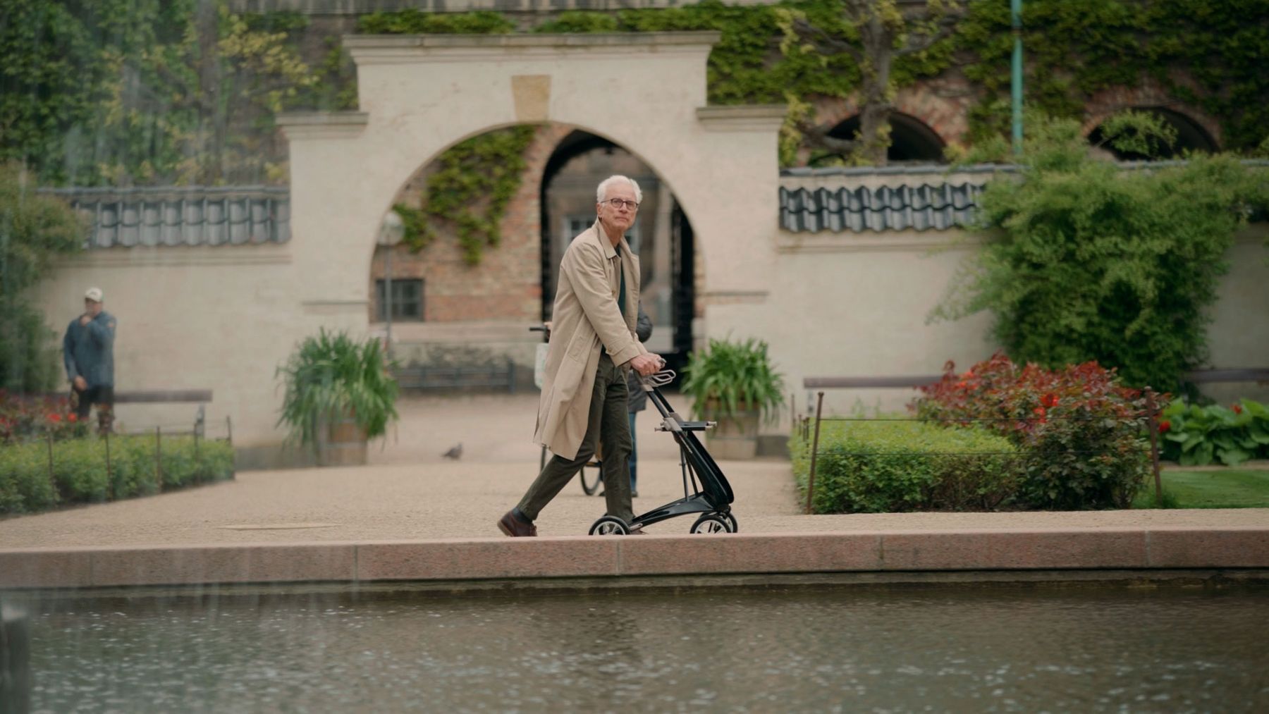 An older man walking in a garden with a lightweight rollator
