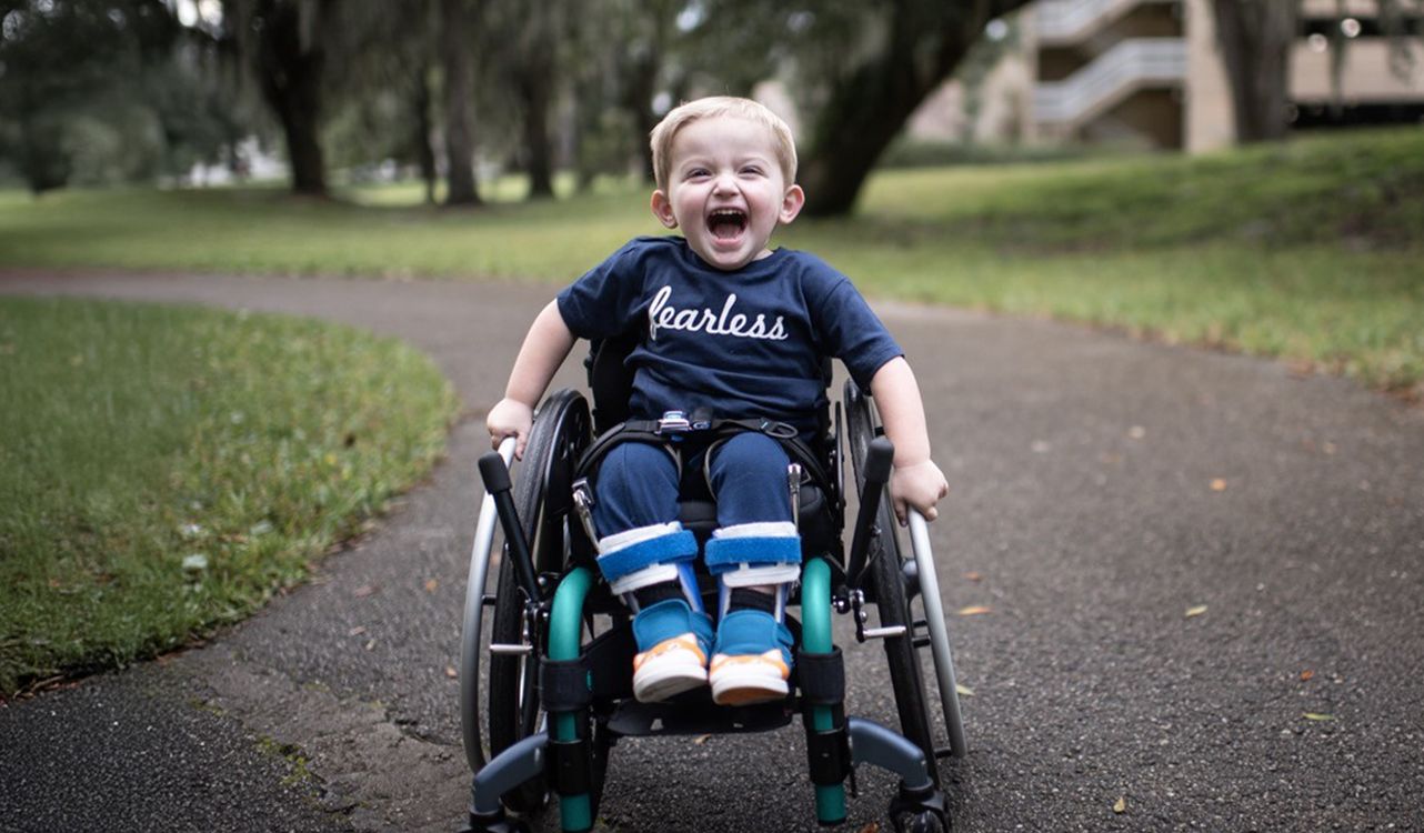 A boy in a paediatric wheelchair on a park path
